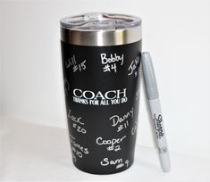 a black and silver tumbler with writing on the side next to a white pen