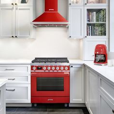 a red stove top oven sitting inside of a kitchen next to white cabinets and drawers