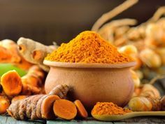 tumerical powder in a bowl surrounded by fresh tumerica and ginger stalks