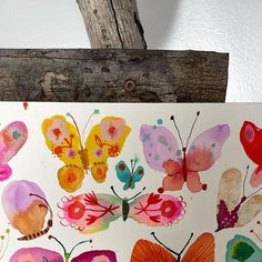 a painting of colorful butterflies is displayed on a piece of wood next to a branch