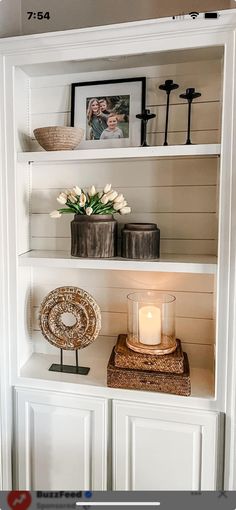 a white book shelf with candles and pictures on it