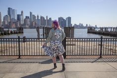 a woman with purple hair is standing near the water and looking out at the city