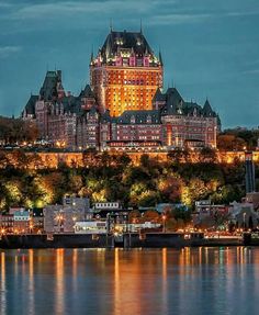 a large building sitting on top of a hill next to the water with lights on it