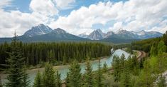 a river surrounded by trees and mountains under a blue sky with white clouds in the background