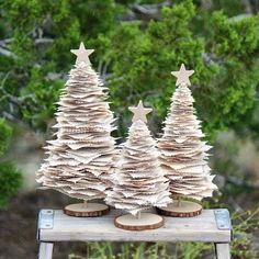 three small christmas trees made out of old book pages on a table in front of some bushes