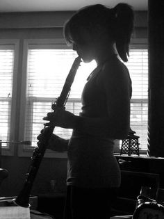 a woman holding a flute in her hands while standing next to a window with blinds