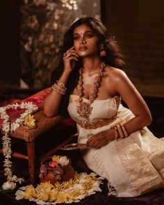 a woman in a white dress sitting on a chair with jewelry around her neck and holding a phone to her ear