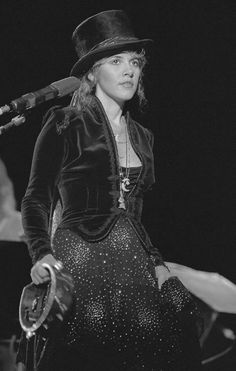 a woman wearing a hat and holding a microphone in her hand while standing on stage