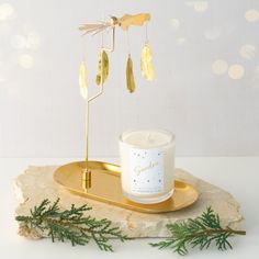 a candle on a tray next to a branch with some gold leaves hanging from it