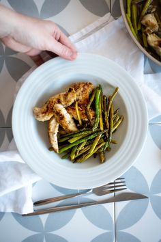 a white plate topped with chicken and asparagus next to a bowl of green beans