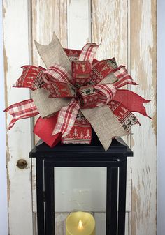 a lantern with a red and white bow on it next to a candle in front of a door