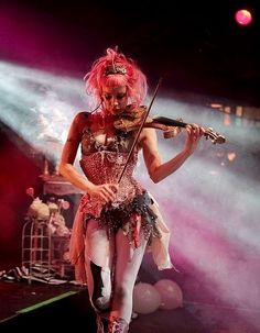 a woman with pink hair playing violin on stage