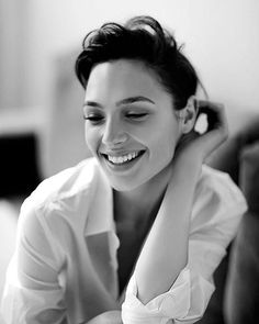 a woman smiling and holding her hair in one hand while wearing a white shirt on the other