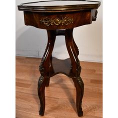 an antique wooden table with glass top and gold accents on the legs, sitting on a hard wood floor