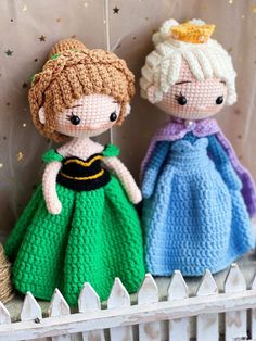 two crocheted dolls sitting next to each other on a white shelf in front of a curtain