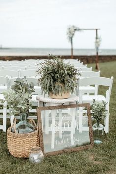 an outdoor ceremony set up with white chairs and greenery in vases on the grass