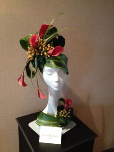 a white mannequin head with red flowers and greenery on it's head