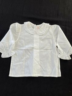 This listing is for a La Luna Firenze NWOT blouse size 6 months. It is a beautifully made 100% finely woven featherweight cotton fabric in bright white. It has a a Peter Pan collar with a ruffled, scalloped embroidered edge. The wrists are embroidered. This blouse buttons down the back. I automatically combine shipping for multiple purchases by the same buyer Fitted White Swiss Dot Top, Fitted Top For Baptism In Spring, Fitted Tops For Baptism In Spring, White Broderie Anglaise Blouse With Peter Pan Collar, Elegant White Shirt With Broderie Anglaise, Classic White Broderie Anglaise Tops, Classic White Tops With Broderie Anglaise, Classic White Tops With Peter Pan Collar, Classic White Top With Peter Pan Collar