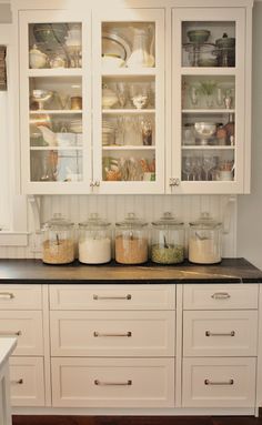 a kitchen filled with lots of white cupboards next to a counter top covered in jars and pans