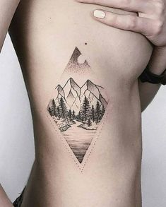 a woman's stomach with mountains and trees tattoo on her side ribcage