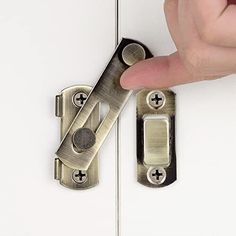 a person's finger is pressing the latch on a white cabinet door with two handles