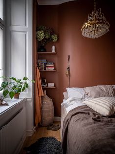 a bed sitting next to a window in a bedroom under a chandelier on a wooden floor