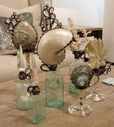 several glass vases with shells and seashells in them on a coffee table