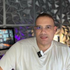 a man wearing glasses and a white shirt is standing in front of two televisions