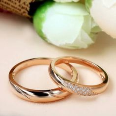 two gold wedding rings sitting next to each other on top of a white table with flowers