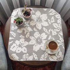 a table topped with two cups of coffee next to potted plants on top of a wooden table