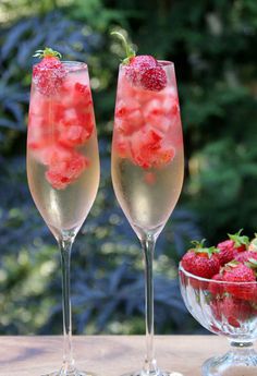 two champagne flutes with strawberries in them sitting on a table next to a bowl of berries