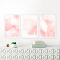 three pink watercolor paintings hanging on the wall next to a white shelf with books