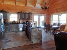 a kitchen and dining area in a log cabin style home with wood floors, stone counter tops, and stainless steel appliances