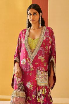 Majenta pheran kaftan with all over floral print, highlighted with zardozi, sequins and jute. Paired with a coordinating floral print joggers and lime green bustier
Components: 3
Pattern: Embroidery, Print
Type Of Work: Zardozi, Sequins, Jute, Floral
Neckline: Deep V Neck
Sleeve Type: Flared Sleeves
Fabric: Silk, Lurex
Color: Pink
Other Details: 
Zardozi embroidered patch-pocket with tassels
Note:
Potli bag held by the model is not for sale
The pink outfit worn by the other model is not for sale Priyanka Singh, Potli Bag, Embroidery Print, Embroidery Floral, Pattern Embroidery, Printed Joggers, Silk Embroidery, Fabric Silk, Jogger Set