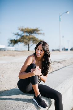 a woman sitting on the side of a cement wall with her arms crossed and smiling