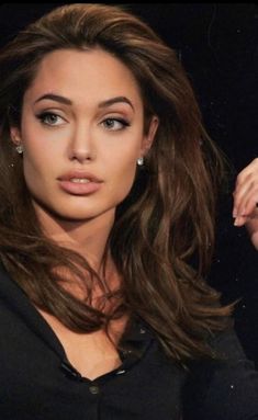 a woman with long brown hair posing for a photo in front of a black background