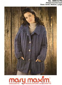 a woman wearing a blue knitted jacket and sweater in front of a wooden wall