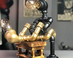 a gold and black robot made out of pipes on top of a wooden table next to a lamp