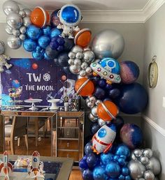 a room filled with lots of balloons and space themed decorations on the wall, including an astronaut balloon arch