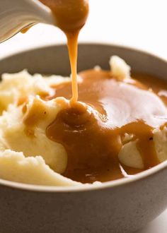 a spoon drizzling gravy over mashed potatoes in a bowl