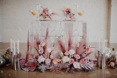 a clear box with flowers and feathers on the top is surrounded by other glass vases