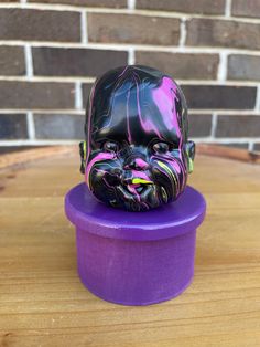 a purple hat box with a black and pink mask on it's head sitting on top of a wooden table