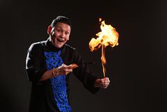 a man in black shirt holding a stick with fire coming out of it and smiling at the camera