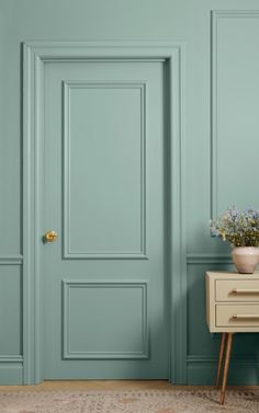 an empty room with green walls and a white table in front of the door that has a potted plant on it