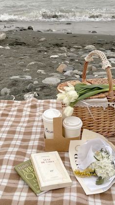 there is a basket with flowers and books on the table next to the water's edge