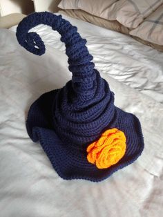 a crocheted blue hat with an orange flower on the side sitting on top of a bed