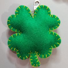 a green flower shaped keychain hanging from a hook on a white wall with yellow stitching