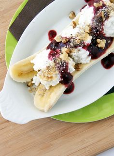 a banana split with whipped cream and blueberry sauce on a green and white plate