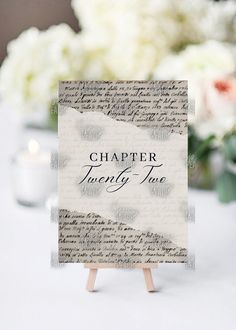 a table topped with a card next to a vase filled with white flowers and greenery