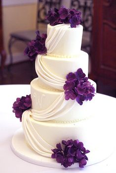 a three tiered white cake with purple flowers on top